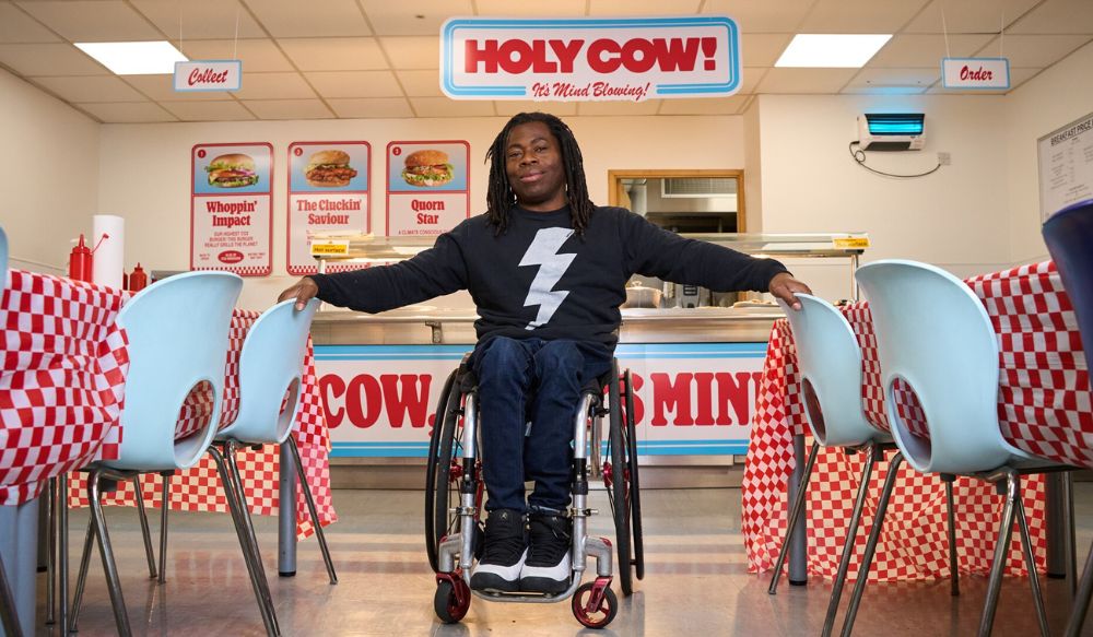 Man in a wheelchair in a diner-style cafe with 'holy cow' sign hanging from ceiling